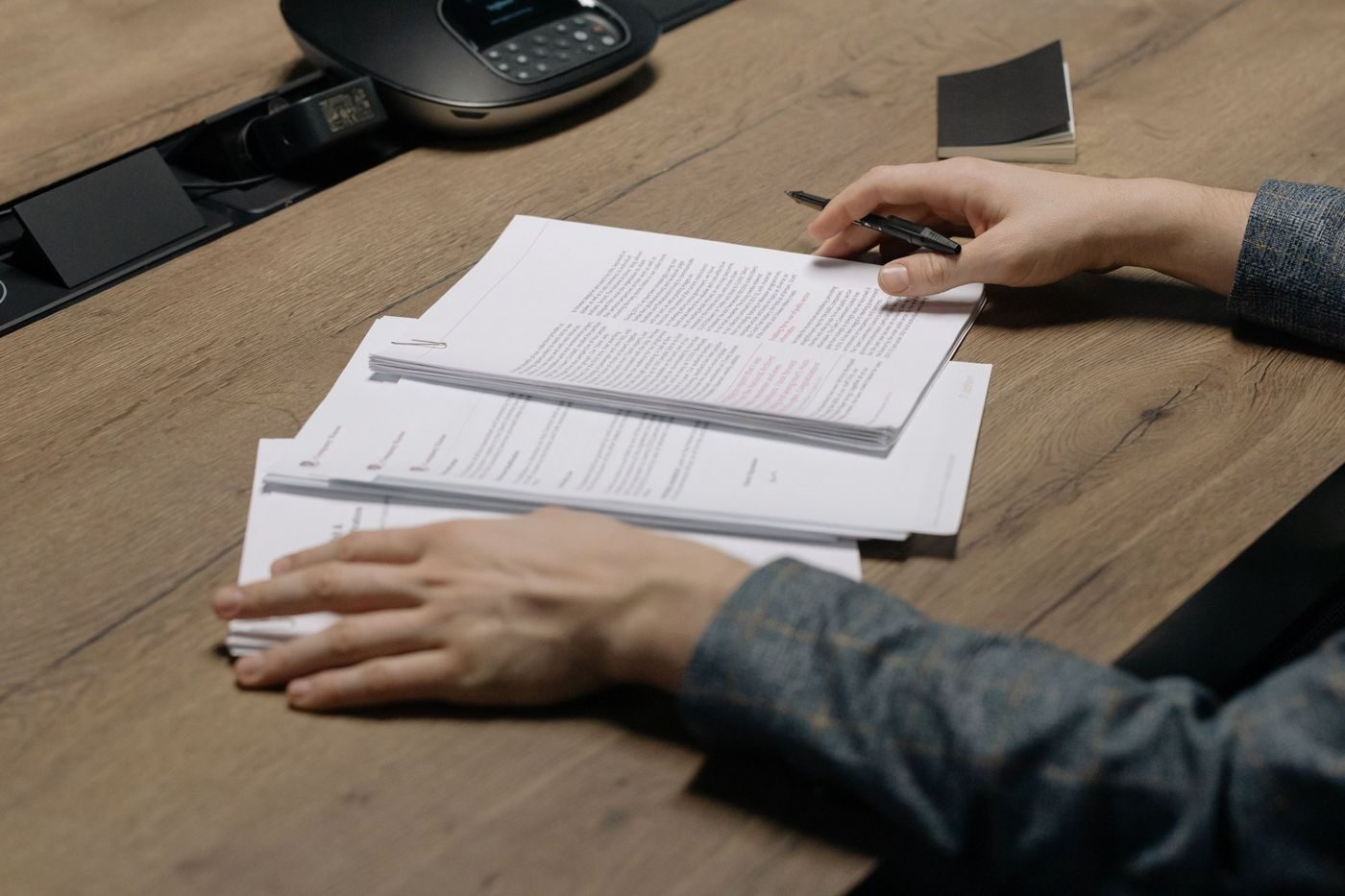Hands reviewing a stack of printed documents with a pen on a boardroom table